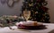 Wineglass and plates on served or setted table for christmas celebration. Empty dininng room with fir tree blurred on background.