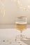 Wineglass with sparkling wine alcohol drink on beige linen tablecloth with natural shadows and gold confetti, blurred