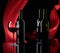 Wineglasses and bottles of red wine on a black reflective background. Red satin curtain flutters in the wind