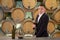 Winemaker inspecting quality of red wine, standing near bottles racks in winery vault