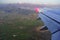 Wing of a flying plane against the background of the earth, fields, houses and green mountains of Montenegro