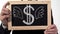 Winged dollar symbol drawn on blackboard in businessman hands, growth of prices