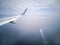 Wings of the plane during the flight look from the passenger window. There are not many white clouds in the blue sky above the gro