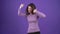 The winning charismatic woman shouts hands up, shows the like sign. Brunette isolated on a purple background, dressed in