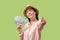 Winning the lottery. A young Caucasian happy woman hold a fan of dollars and point index finger. Light green background