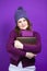 Winsome Adult Caucasian Woman in Warm Knitted Hat and Purple Scarf Posing with Big Wrapped Giftbox Whie Embracing Box With Both