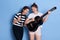 Winsome ladies with knot and pigtails singing songs and playing guitar, having fun together, preparing for music competition,