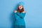 Winsome young romantic woman with red wavy hair expresses self love and care, tilts head, wears blue jumper and cap, embraces own