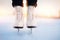Winter active holiday concept. Woman standing on ice in white figure skates, snow flakes sunset