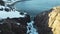 Winter aerial flight through scenic canyon top over waves rolling on artic ocean shore with round stones, ocean waves at