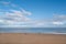 A winter beach on a blue sky day with fluffy white clouds. A few unrecognisable people are walking on the beach