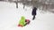 Winter behind follow father pulling red bobsled on snowy field with child.Dad, son or daughter, bobsleigh on snow.Family