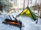 Winter Camping Adventure in Snowy Forest With Warm Campfire and Green Tent