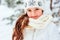 Winter close up portrait of cute dreamy child girl in white coat, hat and mittens playing outdoor in snowy winter forest