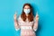 Winter, coronavirus and social distancing concept. Cute hopeful girl with red hair, wearing face mask, cross fingers and