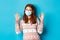 Winter, coronavirus and social distancing concept. Satisfied redhead girl praising good thing, wearing medical mask