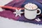 Winter cozy concept. Coffee with marshmallows and decorative shiny snowflake in white enameled metal cup in purple warm wool scarf