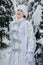 Winter day. Girl in the costume of the Snow Maiden in the forest on a background of snowy trees. New Year`s Eve, Christmas