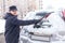 Winter driving. The man is cleaning car\'s window from snow.