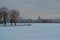 Winter embankment of Saint Petersburg with colorful neat buildings stands on banks of frozen Neva river in snow. Park with bare tr