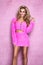 Winter fashion. Beautiful happy blonde woman in pink outfit on a pink plush background. The model is wearing a stylish  cozy pink