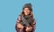 Winter fashion. Beautiful young woman wearing woolen sweater, knitted beanie hat and scarf on blue studio background