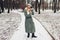 Winter fashion. Young woman wearing long green coat with scarf, hat, mittens and boots in snowy park