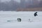 Winter fishing on a little, natural, frozen lake, covered with snow, ice auger, plastic box, rods and thermos, fisherman figure