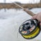 Winter fly fishing picture. Fly rod and reel on snowy river bank