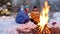 Winter forest. Family sitting in the woods by the fire. Frying sausages on skewers