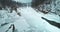 Winter forest frozen river is covered with snow, aerial view. Cold landscape, bridge in distance.