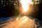 Winter forest, icy snow-covered road and beaming rays of sunset landscape