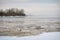 Winter freezing sea with ice floes. A small island with dark gloomy forest in the distance. Northern cloudy day, tranquility of