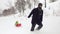 Winter front follow father pulling red bobsled on snowy field with child.Dad, son or daughter, bobsleigh on snow.Family