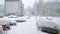 Winter is here. Snowfall in the city. White snow covered cars, parked on a road near apartment buildings. Frosty cold weather, bli