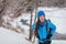 Winter hiking Asian woman hiker walking on snow hike trail in forest outdoors. Backpacking camper with blue down jacket