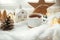 Winter hygge. Stylish cup of tea with modern cute christmas houses, pine cone, wooden star and tree, golden lights on soft warm