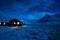 Winter image of a wooden house with light from the window. Landscape with moonlight on the snow with mountains in the background.