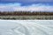 Winter landscape with car ruts in the deep snow, blue sky and pine forest covered with snow