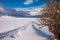 Winter landscape, footprints path and fence on snow valley in bright sunny day