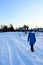 Winter landscape on frosty sunny morning. Girl in warm clothes walks along snow-covered path. Rear view.