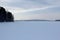 Winter landscape on a frozen lake, forest on the hills in the background. The snowy expanse extending into infinity