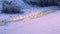 Winter landscape with a frozen river bank line, a golden streak of water and a line of footprints in the snow.