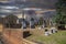 a winter landscape in the graveyard with headstones, graves, bare trees, lush green trees, plants and flowers