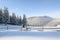 Winter landscape. The meadow overlooks the mountains, the forest with trees covered with snow and the blue sky. On the path near