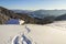 Winter landscape of mountain valley on frosty sunny day. Footprint path in white deep snow leading to small old wooden shepherd