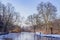 Winter landscape with a pond with its frozen waters, frost and snow, surrounded by huge bare trees