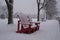 Winter landscape - red Muskoka adirondack wooden chairs in city park in heavy snowstorm