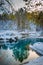 Winter landscape small turquoise lake in the mountains among snow-covered forest. Trees are reflected in the lake water. Vertical