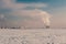 Winter landscape with snow covered frozen ice, city and pipes with thick steam